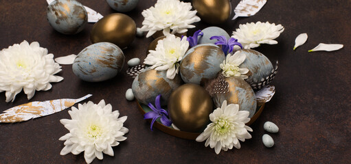 Obraz na płótnie Canvas Easter Decoration with gray blue golden eggs, quail feathers, white flowers on dark wooden background. Selective focus, copy space.