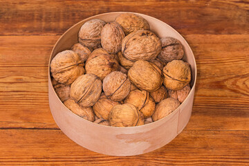 Walnuts in shells in wooden round box on rustic table
