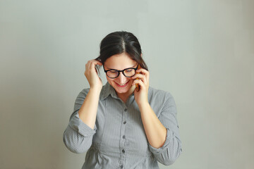 Smiling pretty brunette girl with eyeglasses calling phone and talking isolated over gray background