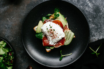 Breakfast. Sandwich with ham, poached egg, avocado and spinach in a plate on a dark background