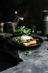 Breakfast. Sandwich with ham, poached egg, avocado and spinach in a plate on a dark background