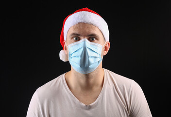 Man in a santa hat and medical mask on a black background.