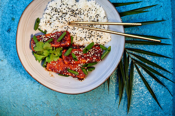 Delicious Korean tofu. Fried tofu in a spicy glaze, sprinkled with green onions and coriander. Served on a beautiful white plate with borders and chopsticks. And it all fits nicely with the blue backg