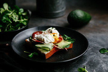 Breakfast. Sandwich with ham, poached egg, avocado and spinach in a plate on a dark background