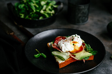 Breakfast. Sandwich with ham, poached egg, avocado and spinach in a plate on a dark background
