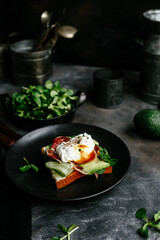 Breakfast. Sandwich with ham, poached egg, avocado and spinach in a plate on a dark background