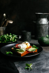 Breakfast. Sandwich with ham, poached egg, avocado and spinach in a plate on a dark background