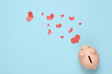 Piggy bank with paper Cut Red hearts on blue background. Top view