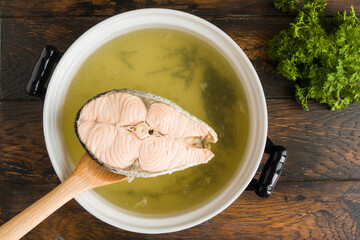 Fish broth in casserole, piece of salmon on spoon, green parsley, top view - 411830451