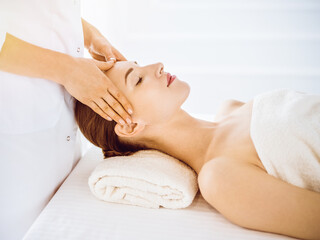 Obraz na płótnie Canvas Beautiful woman enjoying facial massage with closed eyes in sunny spa center