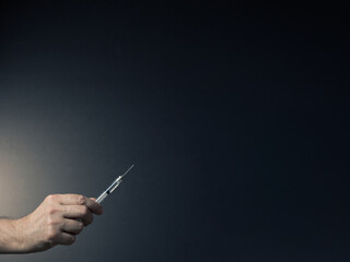 Colour image of man's hand holding syringe upwards in fingertips with dramatic lighting and text space to right