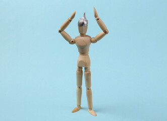 Wooden puppet in a foil hat on a blue background. Conspiracy