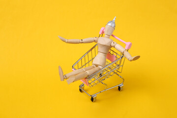 Wooden puppet with foil hat in shopping trolley on yellow background. Conspiracy