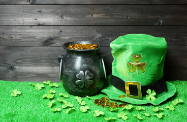 Cast iron pot with treasure and leprehaun hat, clover leaves and coins on green grass, dark wooden planks background. Saint Patricks Day banner, poster, flyer, invitation template