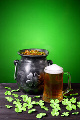 Cast iron pot with four-petal lucky shamrock leaf, mug of beer, clover leaves on dark wooden table and green gradient background. Saint Patricks Day banner, poster, flyer, invitation template