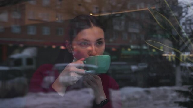 Woman blue protective mask her face from virus sits coffee shop outside window. Looks streets city passers cars drinks coffee tea large mug takes off mask. Social distancing compliance safety measures