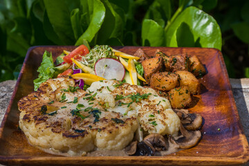vegan cauliflower steak served outside on a wooden plate with green salad and sauteed potatoes