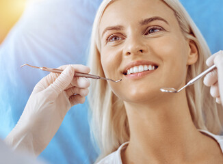 Smiling blonde woman examined by dentist at sunny dental clinic. Healthy teeth and medicine concept