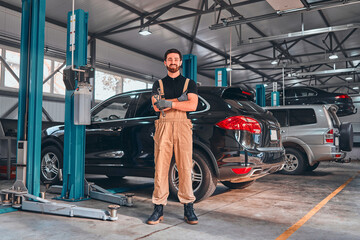 Fototapeta na wymiar A professional male mechanical employee of a car service workshop stand with crossed arms and tools, looks very symphaticly and competently.