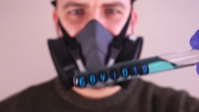 Caucasian Male Scientist Wearing Gas Mask and Blue Latex Gloves while Examining Test Tube With Covid 19 Sample
