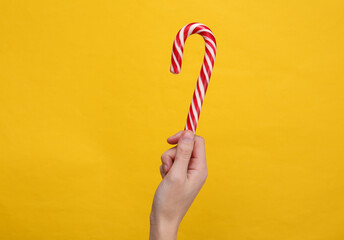 Hand holding Christmas striped candy cane on yellow background.