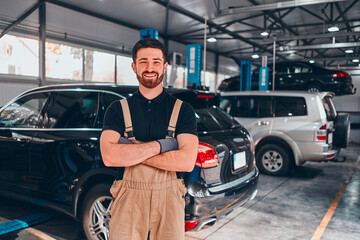 Auto mechanic with crossed arms smiling in his garage.