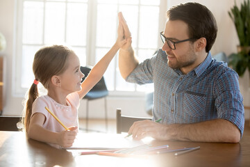 Overjoyed Caucasian father and small cute 7s daughter give five drawing painting together in album...