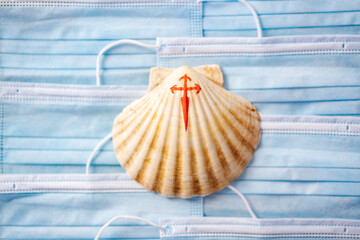 Shell with a painted red cross, symbol of the pilgrim, on a background of blue surgical masks....