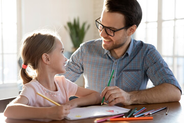 Happy young Caucasian father and little 7s daughter have fun drawing paining together in album....