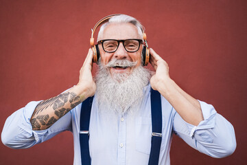 Happy hipster senior man listening to playlist music outdoors - Focus on face