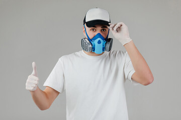 Man in full-faced respirator showing thumb up on grey background.