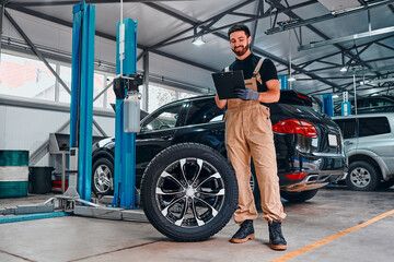 Obraz na płótnie Canvas Concept of working in a car service center. Mechanic notes tire condition, tire tread, lifetime, alloy strength wheels and brake systems for safety.
