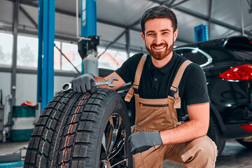 Fototapeta A technician in workwear, holding a wrench and a car tire in tire fitting. obraz