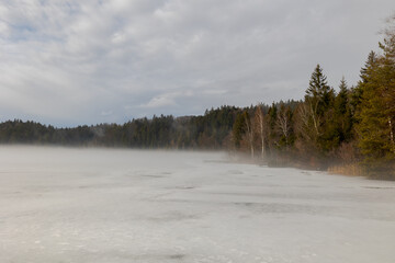 Obraz na płótnie Canvas Frozen lake in dense fog with trees on the shore in Upper Bavaria in winter