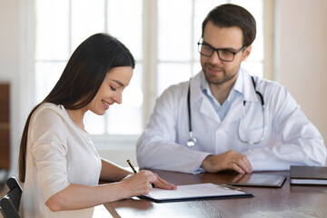 Smiling female Caucasian patient sign paper contract make health insurance agreement with male doctor in clinic. Woman client put signature on document close deal with therapist on private hospital.
