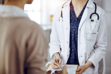 Doctor and patient discussing current health examination while sitting in sunny clinic. Medicine...