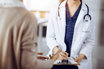 Doctor and patient discussing current health examination while sitting in sunny clinic. Medicine...