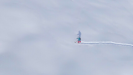 DRONE: Scenic drone shot of wintry landscape surrounding a female ski tourer.