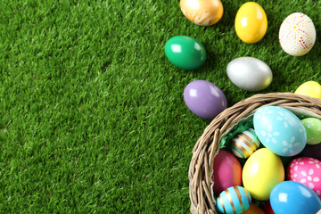 Fototapeta na wymiar Wicker basket with Easter eggs on green grass, flat lay. Space for text