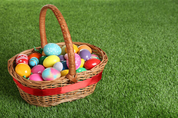 Wicker basket with Easter eggs on green grass. Space for text