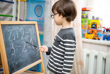 Studying at home. The kid learns to count numbers on the board. Portrait of a cute happy school child boy at home doing homework. Primary school and education.