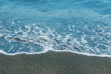 Fototapeta na wymiar White foam wave on the black sand beach close-up