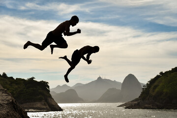 Silhouette of Two Boys Jumping Into the Ocean With Sugarloaf Mountain and Corcovado on Background,...