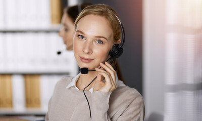 Businesswoman talking by headset while sitting in sunny office. Call center and diverse people group in business