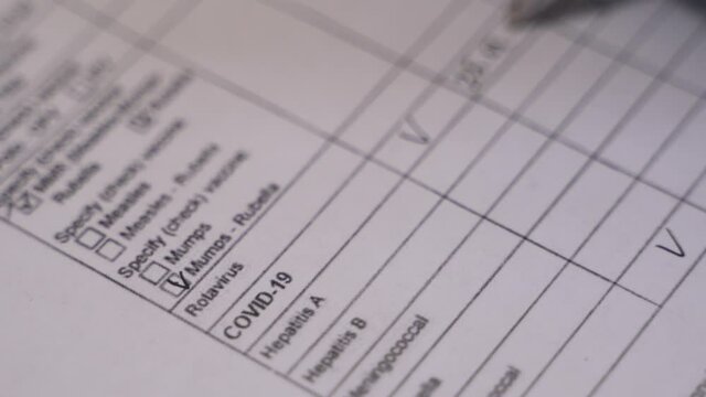 Close up of professional therapist hands signing medical document sitting at the desk in clinic. Doctor filling the vaccination documentation worksheet list during covid-19 pandemic. 