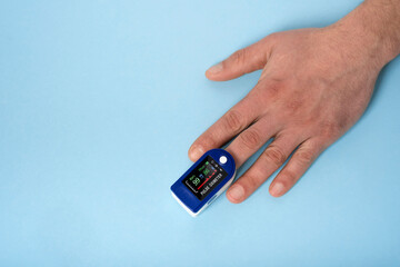 Human hand pulse oximeter used to measure pulse rate and oxygen levels with medical blue background...