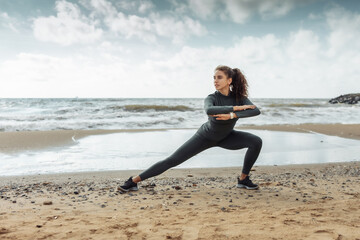 Fototapeta na wymiar Curly sports woman in sportswear doing body warming up or stretching exercise on beach. Healthy lifestyle