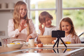 Children In Pyjamas Making Pancakes In Kitchen At Home Whilst On Vlogging On Mobile Phone