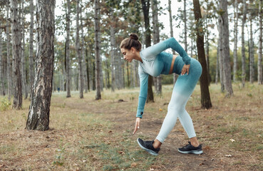 Attractive fitness woman with perfect body doing warm-up or stretching exercise in the forest. Healthy lifestyle