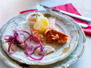 First serving on Swedish christmas food table. Potato, pickled herring, red onion, egg with shrimp, smoked salmon. Cutlery and napkin.